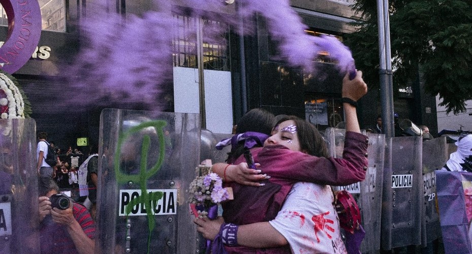Foto de dos mujeres abrazadas sosteniendo una bengala de humo morado